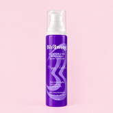 A purple pump bottle of Birdwing Happy Vanilla moisturizing, perfumed body lotion, set against a solid light pink background.